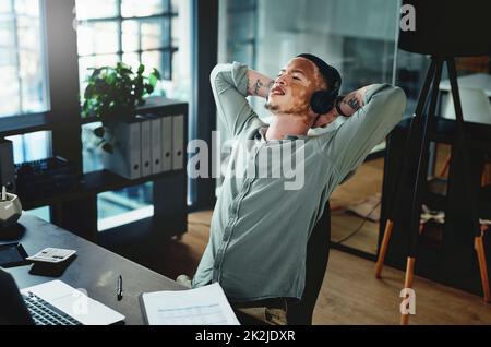 Ascolto del mio podcast preferito. Scatto di un giovane uomo d'affari che indossa le cuffie mentre prende un pisolino in ufficio. Foto Stock