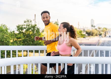 Coppia sportiva interrazziale che corre all'aperto - coppia multirazziale di corridori che indossa abbigliamento sportivo e che fa allenamento funzionale all'aperto per dare forza al corpo Foto Stock