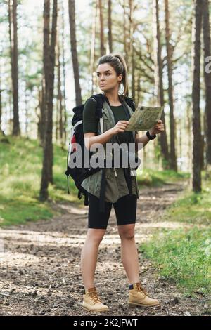 Escursionista femminile con grande zaino utilizzando la mappa per orienteering nella foresta Foto Stock