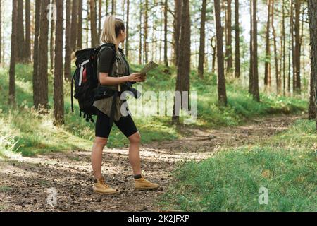 Escursionista femminile con grande zaino utilizzando la mappa per orienteering nella foresta Foto Stock