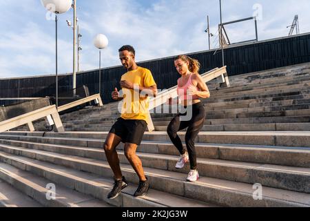Allenamento sportivo interrazziale di coppia all'aperto - coppia multirazziale indossando abbigliamento sportivo e facendo allenamento funzionale all'aperto per tendere i muscoli del corpo, Foto Stock