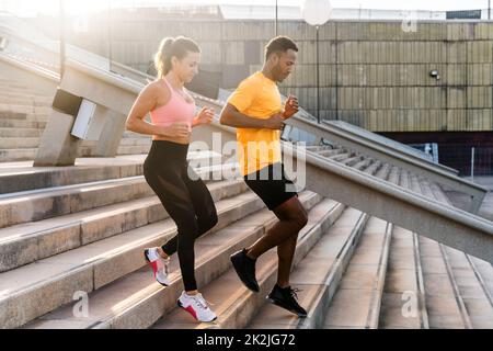 Allenamento sportivo interrazziale di coppia all'aperto - coppia multirazziale indossando abbigliamento sportivo e facendo allenamento funzionale all'aperto per tendere i muscoli del corpo, Foto Stock