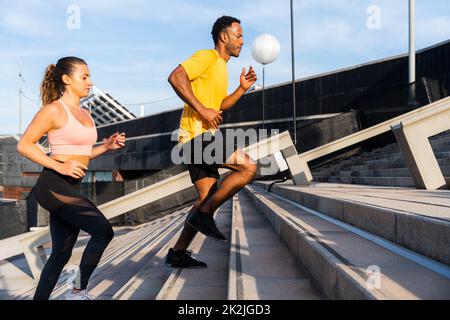 Allenamento sportivo interrazziale di coppia all'aperto - coppia multirazziale indossando abbigliamento sportivo e facendo allenamento funzionale all'aperto per tendere i muscoli del corpo, Foto Stock