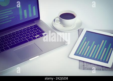 Tutto ciò di cui un uomo d'affari ha bisogno. Scatto ritagliato di un tablet, un notebook e una tazza di caffè su una workstation. Foto Stock