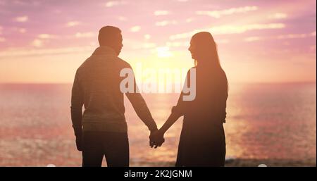 Il tramonto è carino ma youre più bello. Foto retrostensiva di una giovane coppia felice che tiene le mani al tramonto sulla spiaggia. Foto Stock