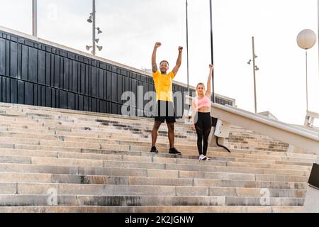 Allenamento sportivo interrazziale di coppia all'aperto - coppia multirazziale indossando abbigliamento sportivo e facendo allenamento funzionale all'aperto per tendere i muscoli del corpo, Foto Stock