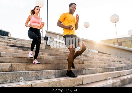 Allenamento sportivo interrazziale di coppia all'aperto - coppia multirazziale indossando abbigliamento sportivo e facendo allenamento funzionale all'aperto per tendere i muscoli del corpo, Foto Stock