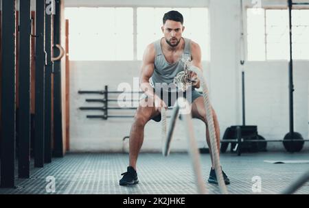 Im sensazione di bruciore. Girato di un giovane uomo utilizzando le corde in palestra per costruire la forza del braccio. Foto Stock