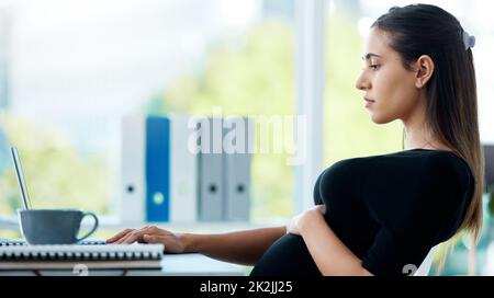 Ottenere alcune scadenze fuori del senso. Scatto di una donna d'affari incinta che lavora su un laptop in un ufficio. Foto Stock