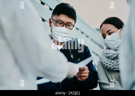 Questo ci permette di viaggiare. Sparato di un giovane uomo che parla con un operatore sanitario in una tuta nocciola durante un focolaio. Foto Stock