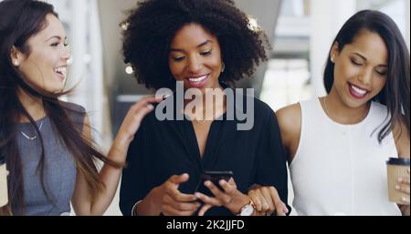 Connessione durante la pausa caffè. Scatto corto di tre giovani belle donne d'affari che camminano attraverso un ufficio moderno. Foto Stock