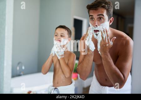 La crema per la rasatura viene sempre prima. Scatto corto di un bel giovane uomo che insegna a suo figlio come radersi in bagno. Foto Stock