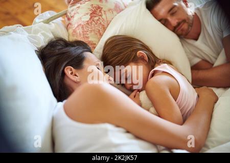 La famiglia si accoccola. Scatto di una famiglia che dorme nel letto di casa. Foto Stock