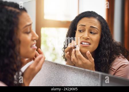 OH no, è che un posto. Scatto corto di una giovane donna attraente che esamina il suo viso in uno specchio nel bagno a casa. Foto Stock