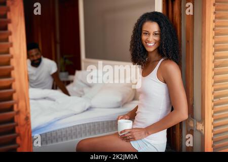 Amore essere a casa insieme. Scatto corto di bella giovane moglie che beve una tazza di caffè mentre il suo marito bello è seduto a letto a casa. Foto Stock