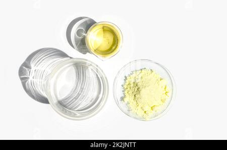 Ingrediente per prodotti chimici cosmetici su tavola bianca da laboratorio. Polvere di zolfo in vetro da orologio chimico e liquido di cloruro di alluminio poli in becher. Vista dall'alto Foto Stock