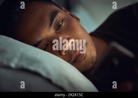 Così tanto per andare a letto presto stasera. Scatto di un giovane uomo sdraiato a letto e con uno smartphone a casa. Foto Stock