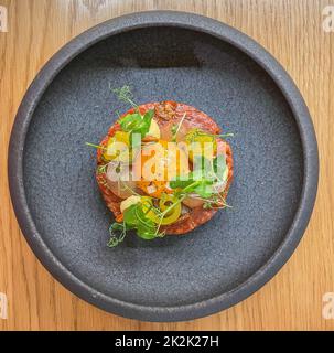 tartare di manzo ben preparato, con un uovo sulla parte superiore e altri ingredienti, servito in un piccolo recipiente - vista dall'alto Foto Stock