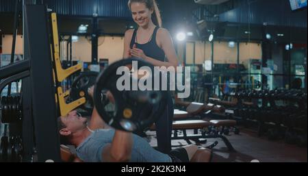 Personal trainer aiutare muscolo uomo banco di pressione sollevamento pesi con Barbell flexing muscoli Foto Stock