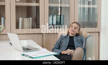 Felice donna d'affari donna sognante mettere le gambe sulla scrivania ha sollevato le braccia in ufficio Foto Stock