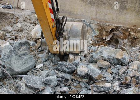 Caricamento di macerie da costruzione con un escavatore in un ambiente polveroso Foto Stock