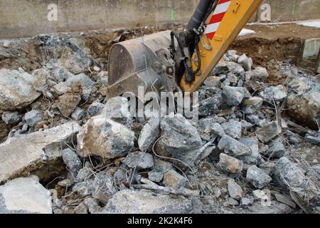 Caricamento di macerie da costruzione con un escavatore in un ambiente polveroso Foto Stock