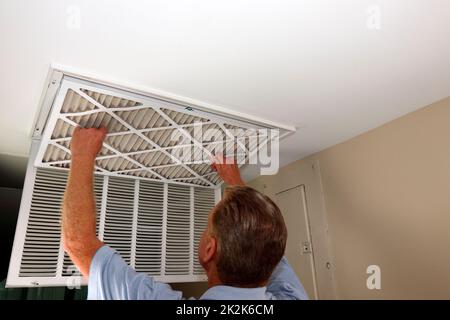 Maschio per adulti per la rimozione del filtro dell'aria da una presa d'aria a soffitto del forno domestico Foto Stock