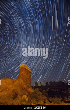 I sentieri delle stelle che ruotano intorno alla North Star su una guglia di arenaria con dipinti leggeri nel Parco Nazionale di Arches, Moab, Utah. Due stelle di tiro sono ali Foto Stock