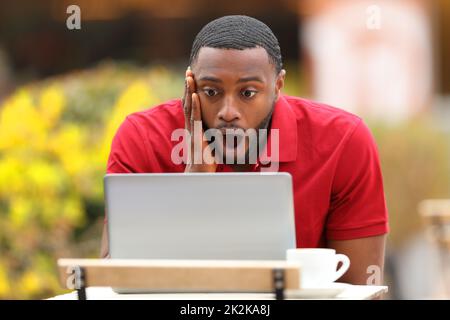 Uomo scioccato con la pelle nera che controlla il laptop in un bar Foto Stock