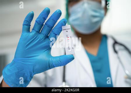 Il medico asiatico in tuta PPE mostra risultati positivi del test con saliva A. Foto Stock