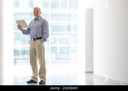 Uomo d'affari senior in piedi che tiene il tablet in alto ritratto tasti Foto Stock