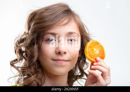 Bambina graziosa che tiene su una fetta di arancia fresca Foto Stock