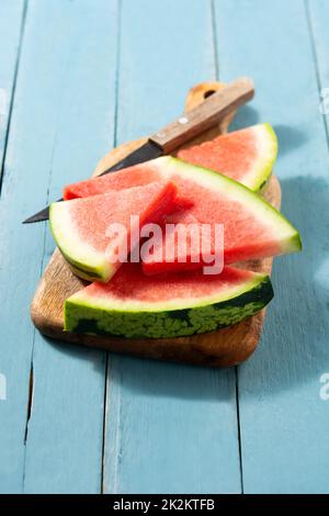 Fette di cocomero fresco sul tagliere e sfondo di tavolo di legno blu Foto Stock