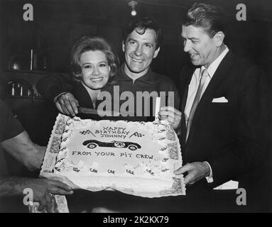 La troupe del film regala al regista una torta di compleanno di suprise. Angie Dickinson, John Cassavetes e Ronald Reagan intorno alla torta. Film: The Killers, USA, 1964 Foto Stock