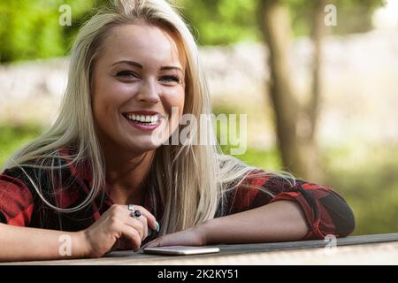 Donna bionda sorridente e felice seduta a un tavolo all'aperto Foto Stock