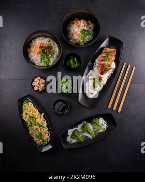 Vari piatti della cucina asiatica con tagliatelle di diversi tipi e riso con gamberi, anatra, verdure e sesamo nero Foto Stock