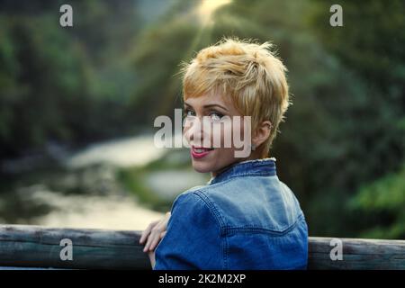 Giovane donna bionda che si rilassa in campagna dal fiume che si gira a voi Foto Stock
