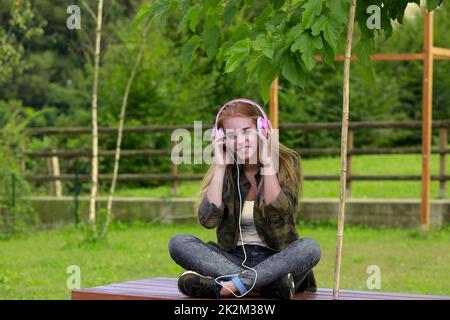 ragazza con cuffie rosa ascolta la musica nel parco Foto Stock