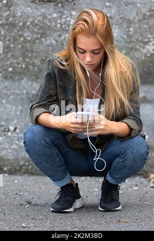 Giovane donna accovacciata ascoltando musica Foto Stock