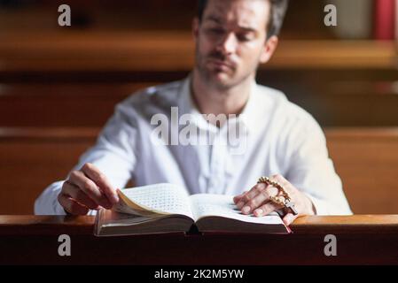 Ascoltare la voce di Dio attraverso il suo verso. Scatto di un giovane che legge la bibbia in chiesa. Foto Stock