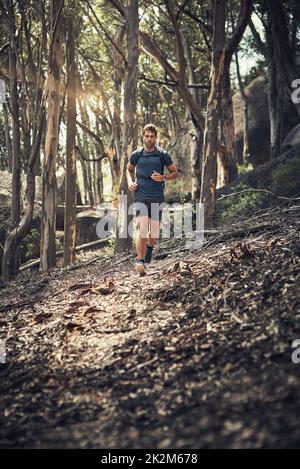 Colpire il sentiero escursionistico a pieno spazio. Scatto a tutta lunghezza di un bel giovane che corre durante la sua escursione in montagna. Foto Stock