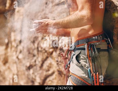 Scalatore di roccia con polvere di magnesio sportiva sulle mani che si prepara a salire sulla scogliera di montagna. Primo piano dell'uomo attivo con gesso di addestramento sul idoneità Foto Stock