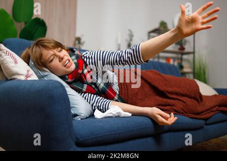 Una giovane donna malata con l'influenza o un'altra malattia chiede disperatamente aiuto sdraiata su un divano a casa Foto Stock