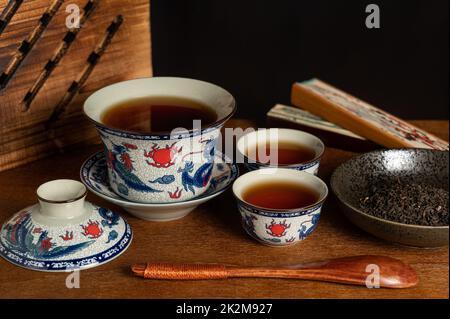 tradizionale tazza da tè in porcellana cinese e foglia di tè su un antico asse di legno Foto Stock