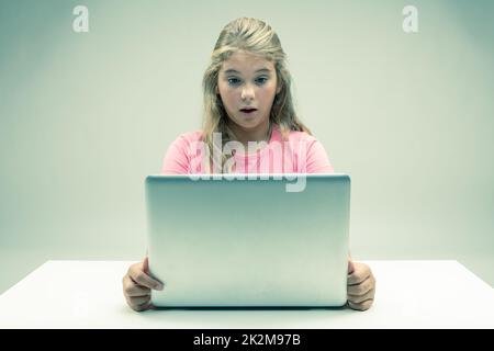 Bambina che fissava il suo laptop con stupore Foto Stock