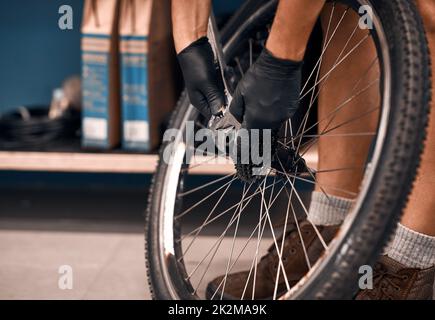 Inferno prendere le ruote di nuovo sulla strada. Scatto corto di un uomo che ripara una bicicletta in un'officina. Foto Stock