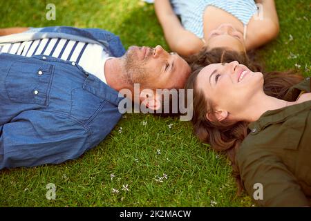 Il tempo con la famiglia è tempo ben speso. Colpo ad angolo alto di una giovane famiglia che si trova sull'erba fuori. Foto Stock