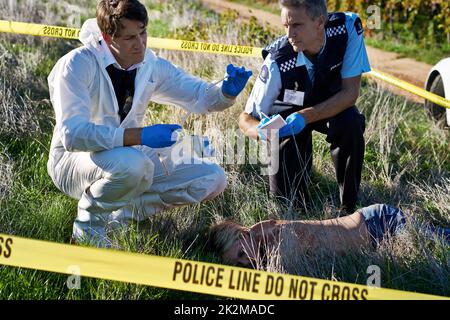 Esame delle prove. Scatto di due investigatori che esaminano le prove ad una scena di crimine. Foto Stock