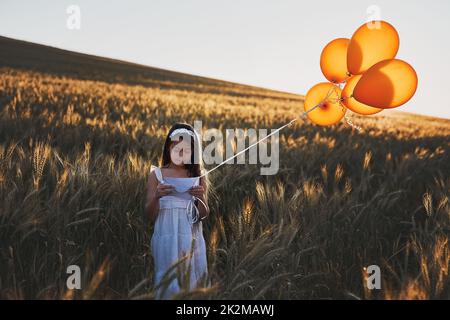 Invio di una lettera sul vento. Sparato di una ragazza piccola carina che attacca una lettera ad un mazzo di palloncini mentre sta in piedi in un campo di mais. Foto Stock