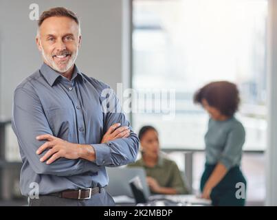 Scopo mortale. Ritratto di un uomo d'affari maturo in ufficio in piedi davanti ai suoi colleghi che hanno un incontro in background. Foto Stock